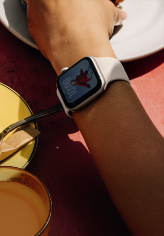 ذراع شخص يمسك طعام الإفطار، Apple Watch SE 3 على المعصم، علبة ألومنيوم Starlight، شاشة تعمل دائمًا، صورة شخص على وجه الساعة، سوار رياضي Starlight