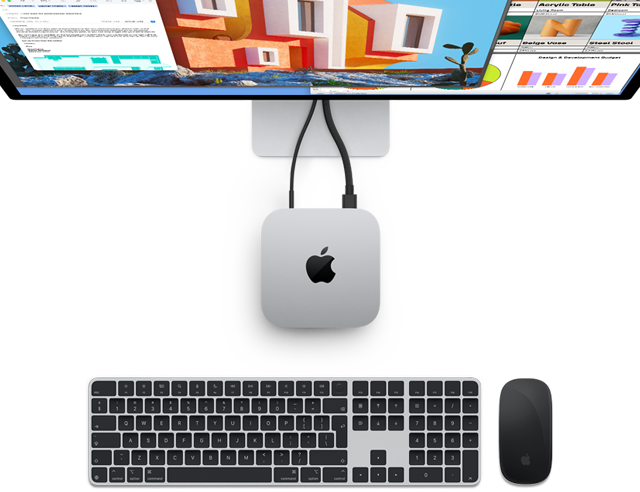 أعلى Mac mini فضي مع شعار Apple، معروض متصل بشاشة وبجانب لوحة مفاتيح Magic Keyboard اللاسلكية وفأرة Magic Mouse